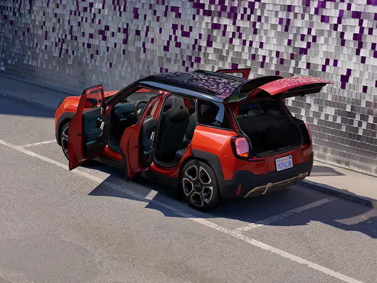 Prikaz stražnjeg kraja potpuno električnog MINI Aceman modela iz ptičje perspektive u Rebel Red boji s krovom u Black boji s otvorenim vratima na ulici.