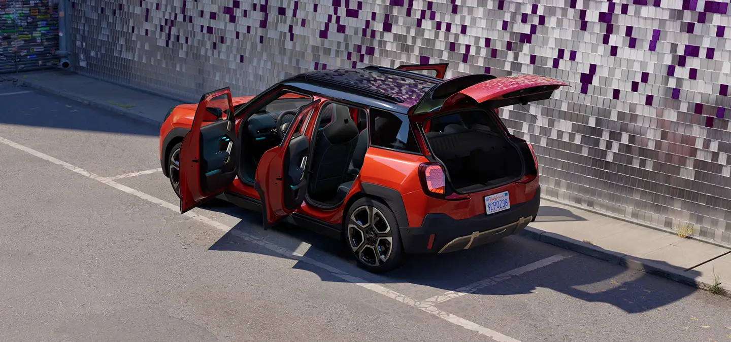 Prikaz stražnjeg kraja potpuno električnog MINI Aceman modela iz ptičje perspektive u Rebel Red boji s krovom u Black boji s otvorenim vratima na ulici.
