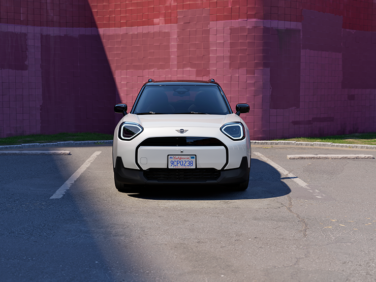 Prikaz prednjeg kraja potpuno električnog MINI Aceman modela u Nanuq White i British Racing Green boji s krovom u Black boji na parkingu.