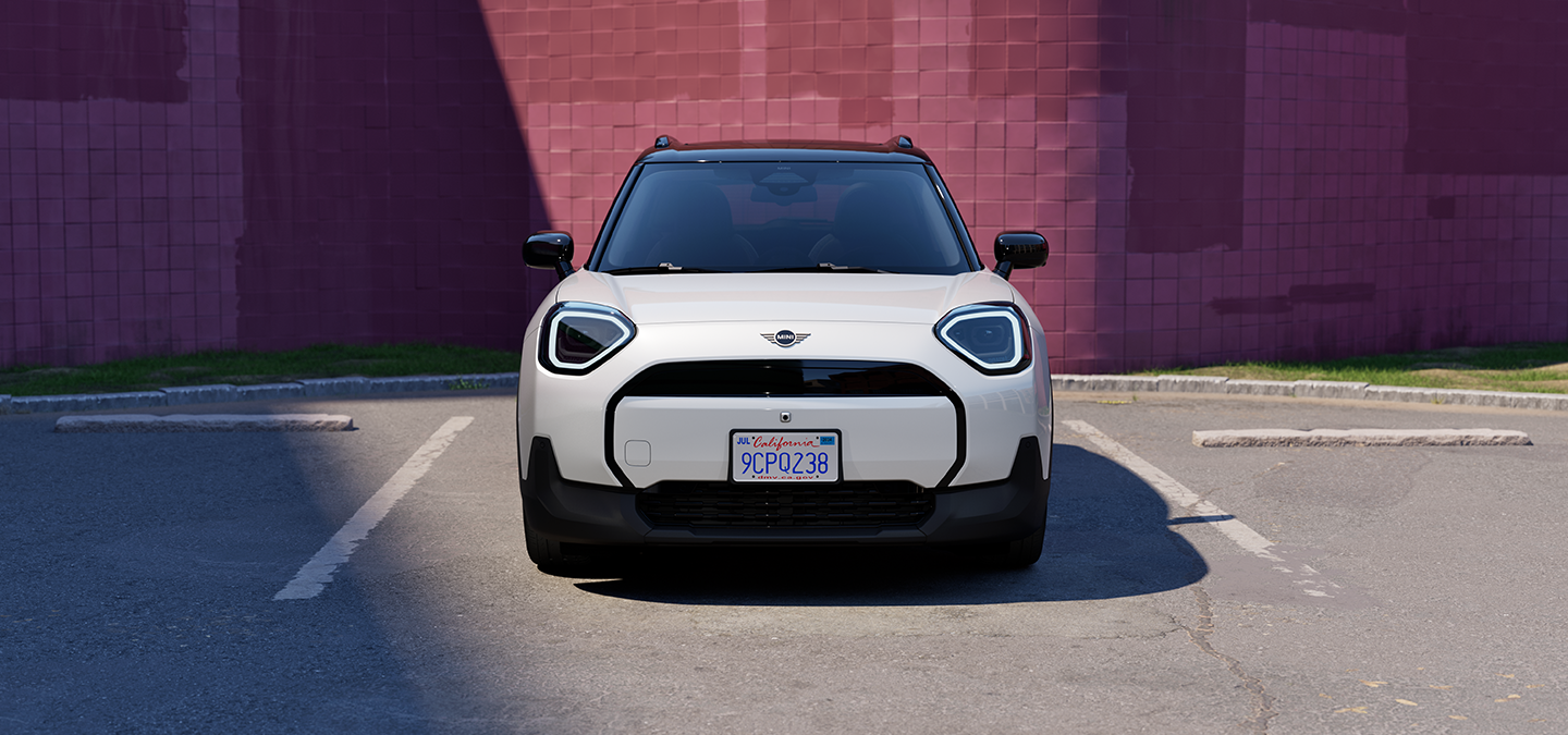 Prikaz prednjeg kraja potpuno električnog MINI Aceman modela u Nanuq White i British Racing Green boji s krovom u Black boji na parkingu.