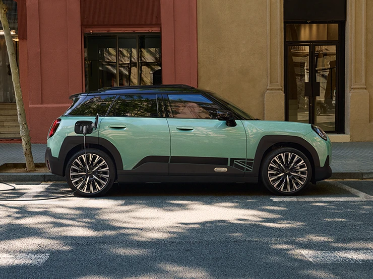 Bočni prikaz potpuno električnog MINI Aceman modela u Ocean Wave Green boji s krovom u Black boji dok se puni na ulici.