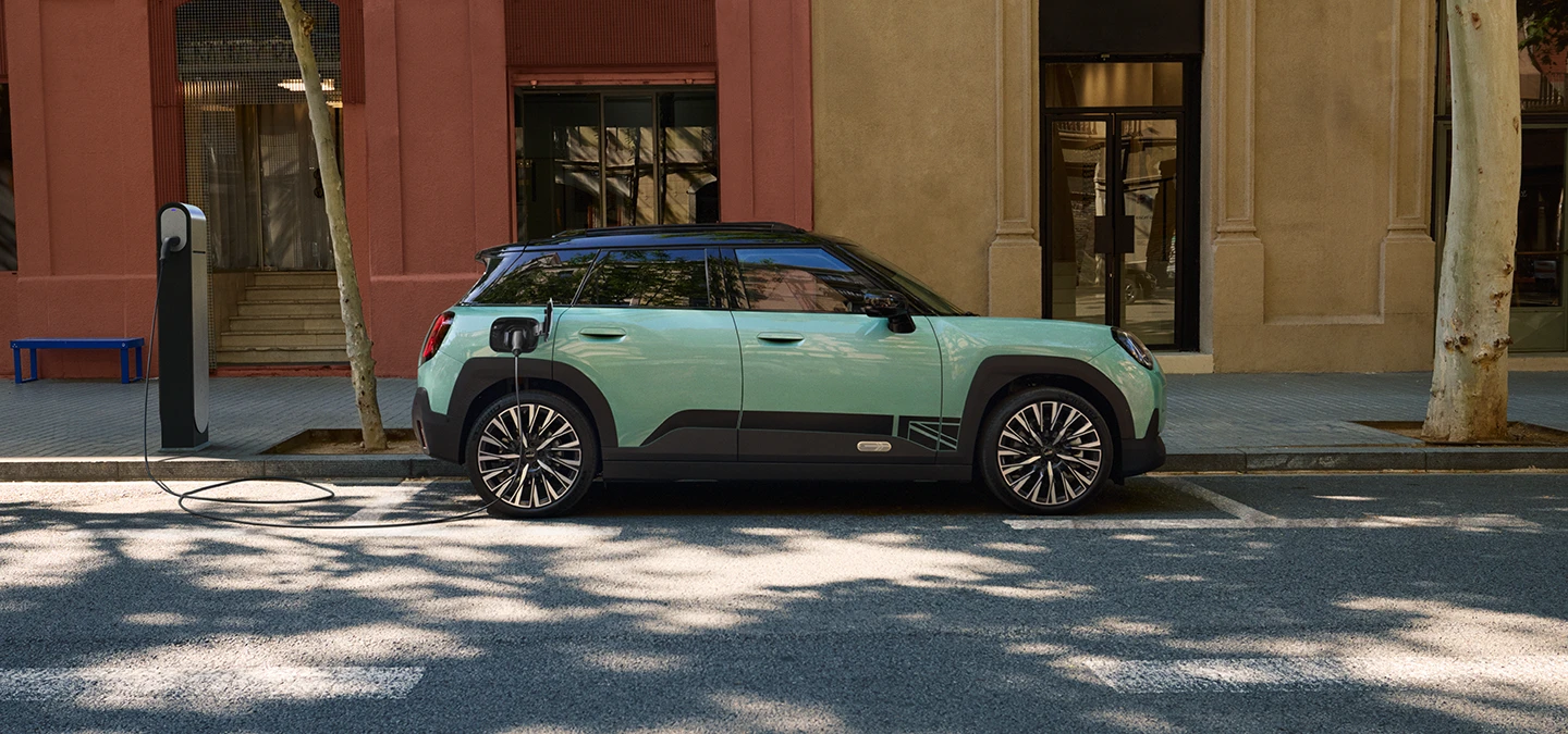 Bočni prikaz potpuno električnog MINI Aceman modela u Ocean Wave Green boji s krovom u Black boji dok se puni na ulici.
