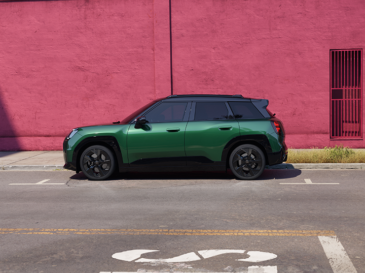 Bočni prikaz potpuno električnog MINI Aceman modela u British Racing Green boji s krovom u Black boji na ulici.