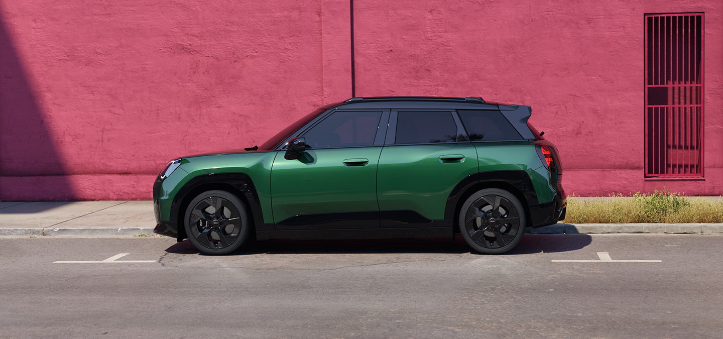 Bočni prikaz potpuno električnog MINI Aceman modela u British Racing Green boji s krovom u Black boji na ulici.