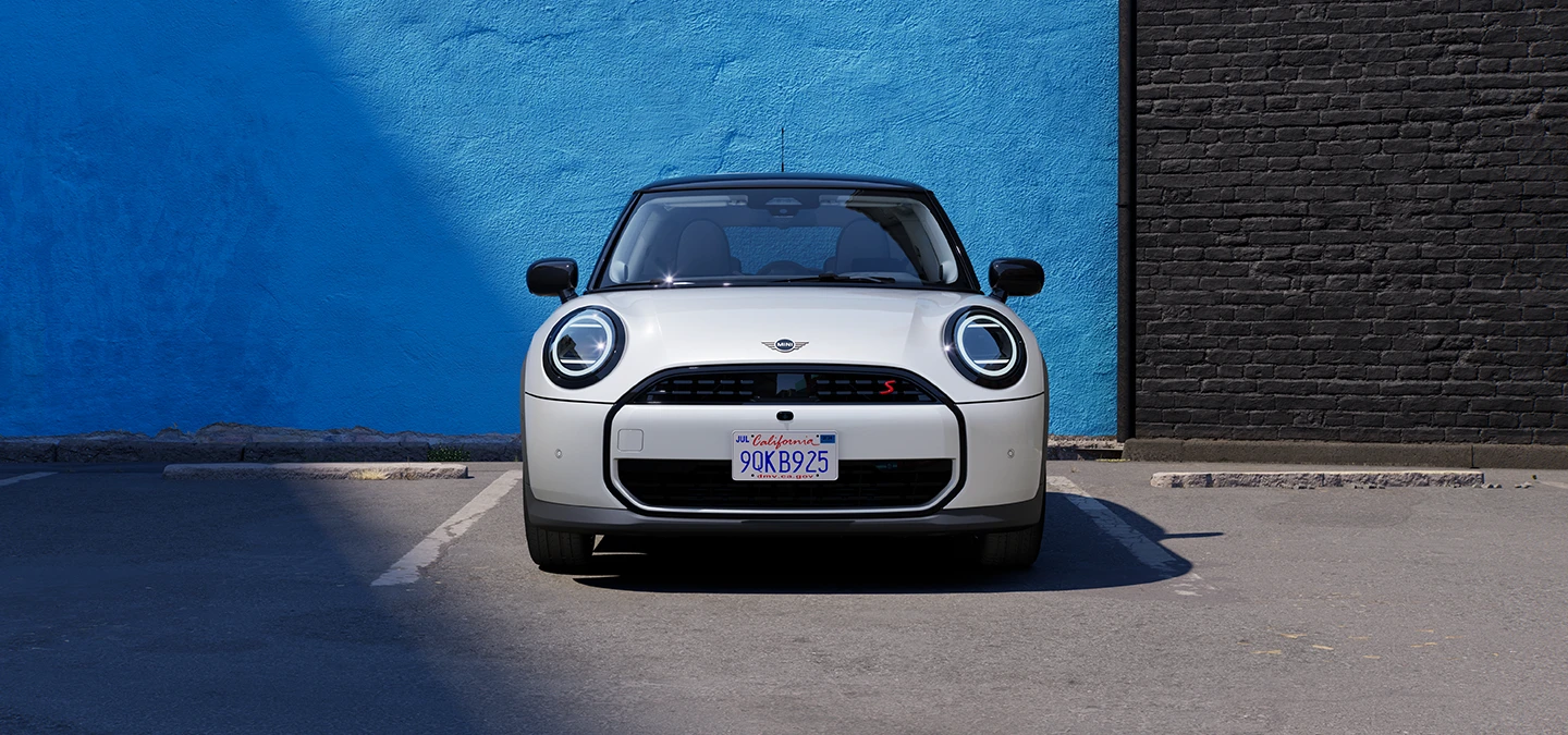 Prikaz prednjeg kraja parkiranog MINI Cooper modela u Nanuq White boji s krovom Black boje.