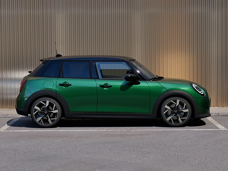 Bočni prikaz MINI Cooper modela s 5-vrata u British Racing Green boji i krova u Black boji na parkingu.
