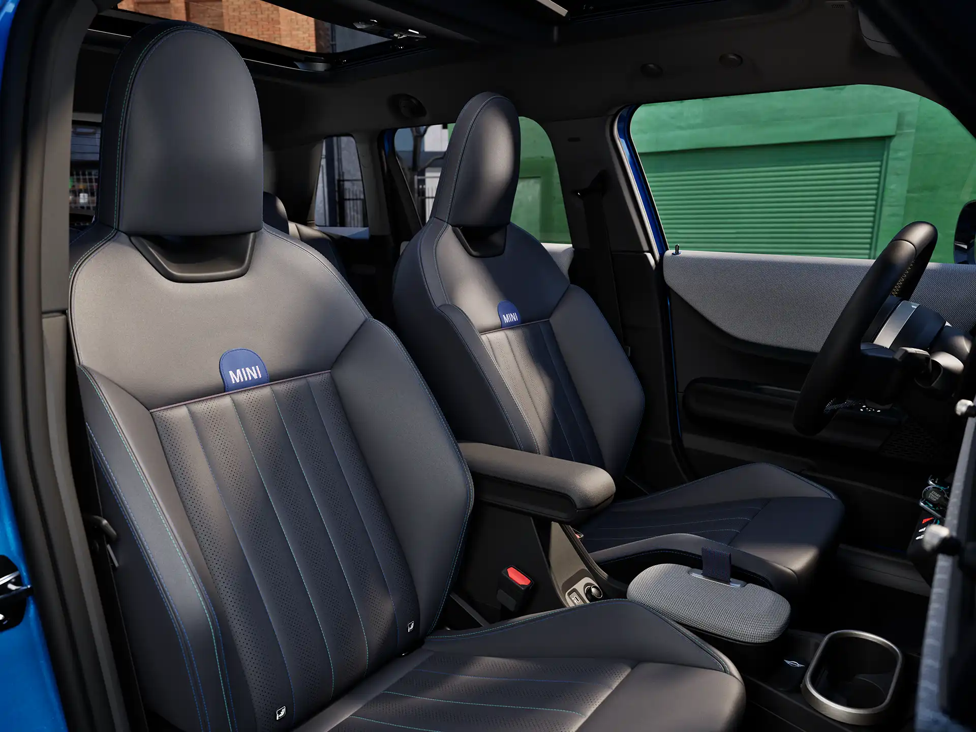 Unutrašnja perspektiva MINI Cooper 5 vrata prikazuje nadzornu ploču, upravljač, okrugli zaslon, panoramski stakleni krov i stražnji dio prednjih sjedala.