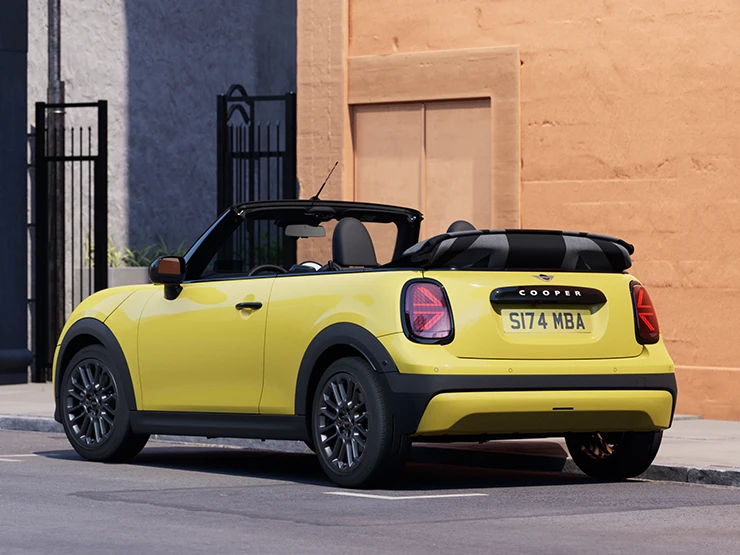 Prikaz lijevog stražnjeg kraja MINI Cooper Cabrio modela u Sunnyside Yellow boji na parkingu.