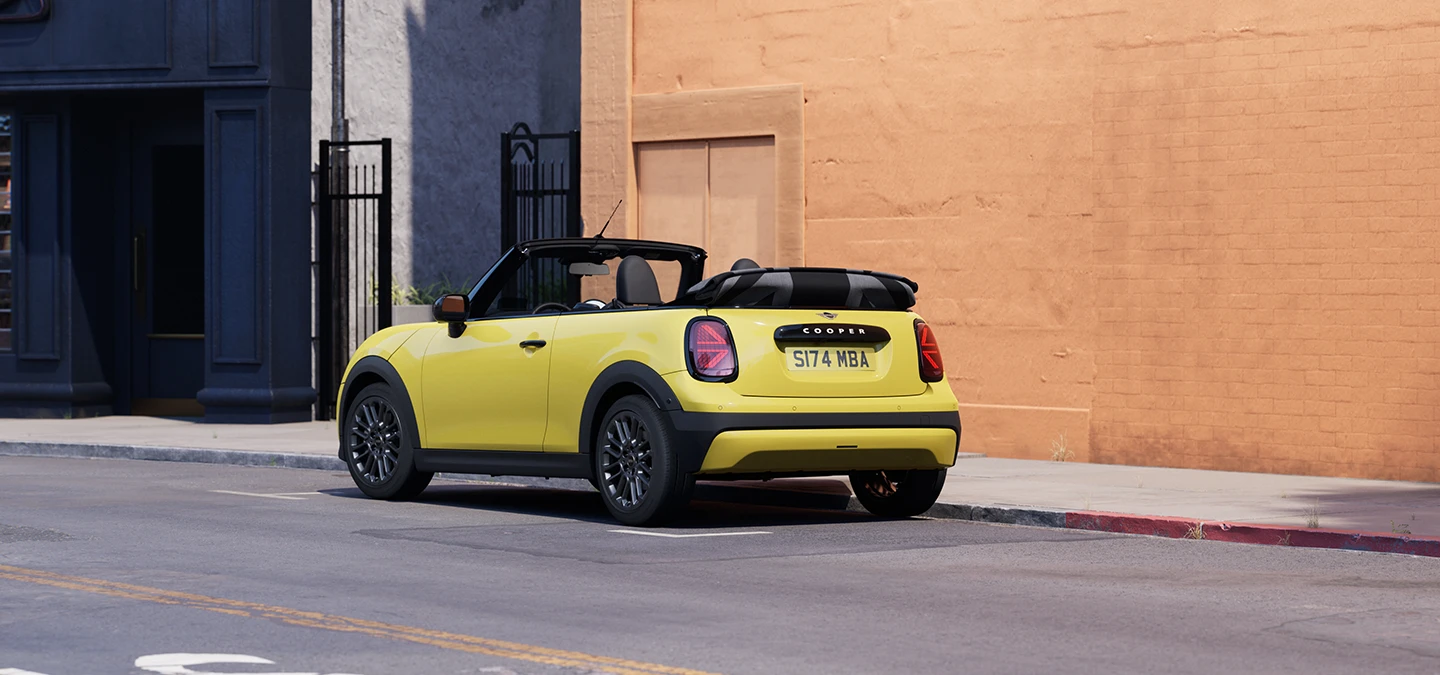 Prikaz lijevog stražnjeg kraja MINI Cooper Cabrio modela u Sunnyside Yellow boji na parkingu.