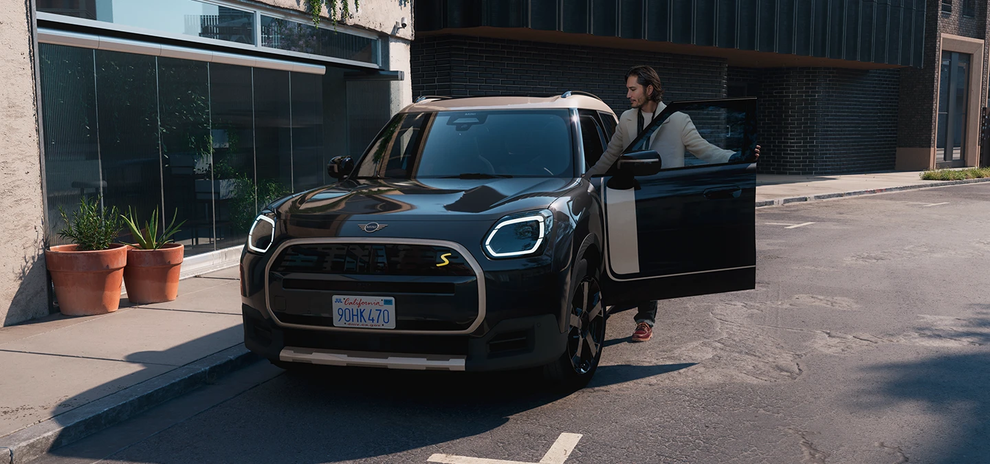 Prikaz prednjeg kraja potpuno električnog MINI Countryman modela u Midnight Black boji i krova u Vibrant Silver Roof boji na ulici.