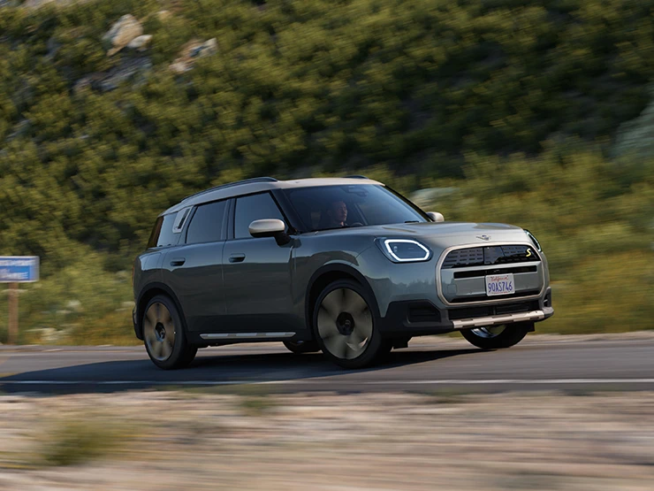 Bočni prikaz stražnjeg kraja potpuno električnog MINI Countryman modela u Smokey Green boji i krova u Vibrant Silver Roof boji u offroad vožnji.