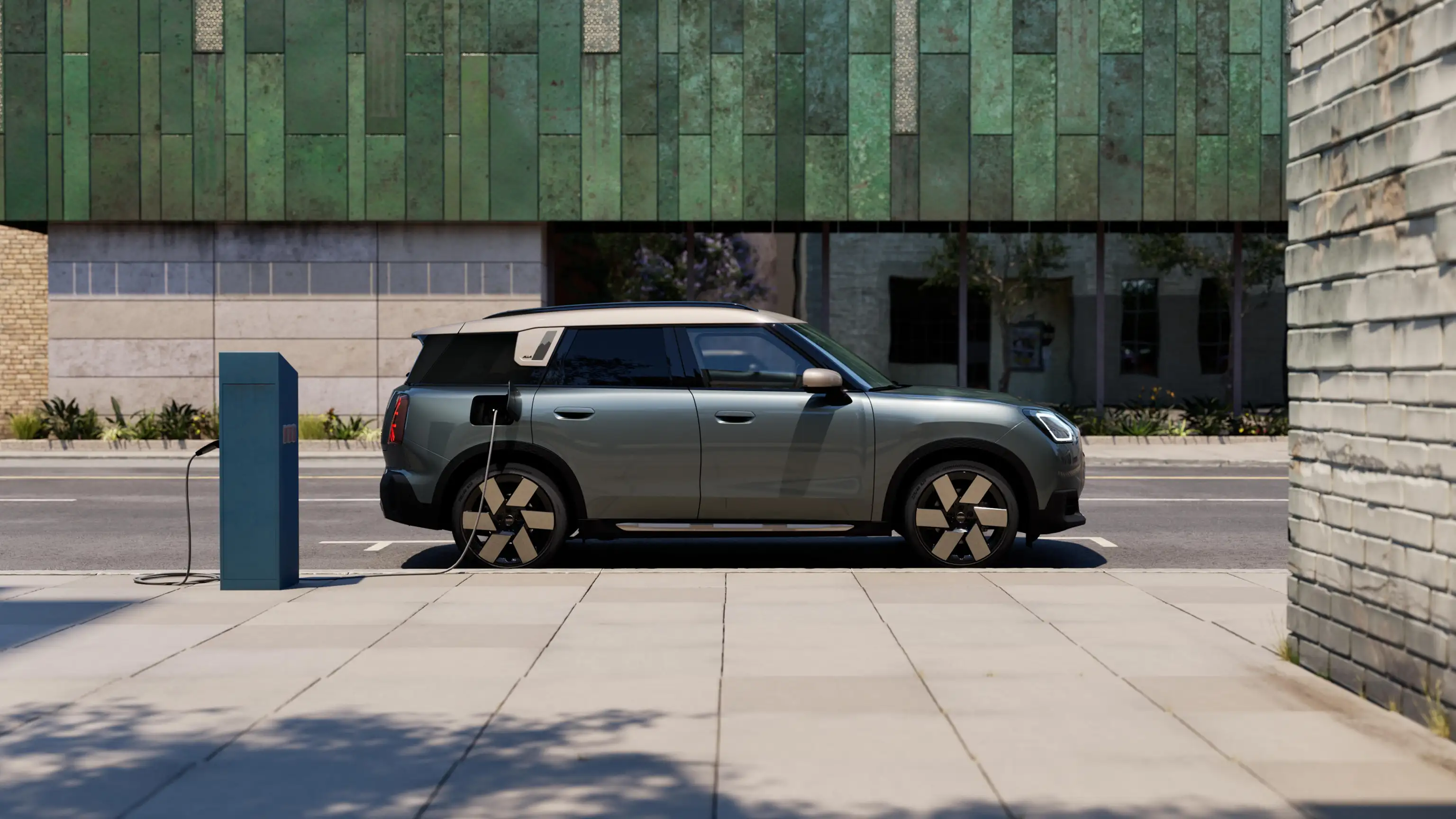 Bočni prikaz na potpuno električni MINI Countryman model koji se puni u Smokey Green boji s Vibrant Silver krovom na ulici