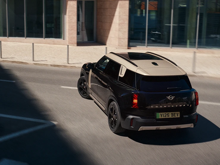 Prikaz stražnjeg kraja potpuno električnog MINI Countryman modela iz ptičje perspektive u Midnight Black boji i krova u Vibrant Silver Roof boji na parkingu