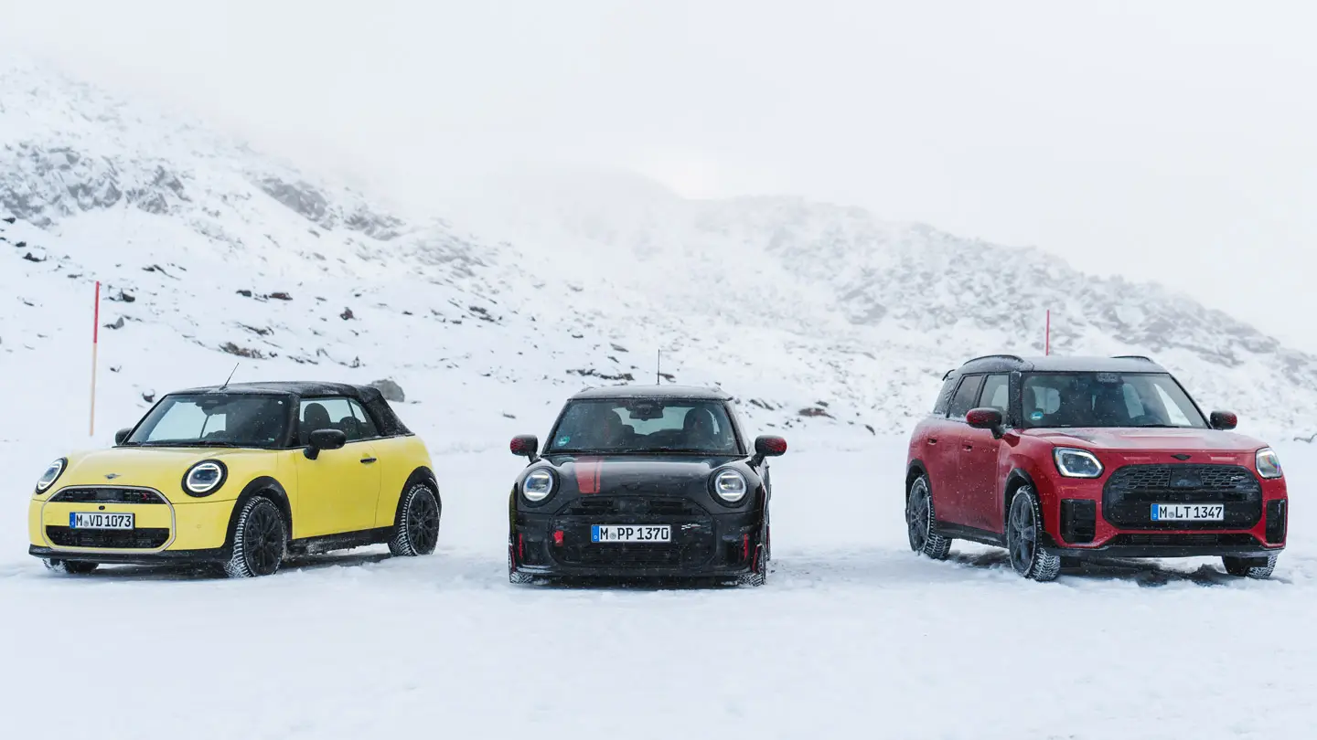 MINI Cooper Cabrio u Sunny Side Yellow boji, MINI John Cooper Works u Midnight Black II boji i MINI Countryman Cooper u Chilli Red boji - stacionarni na snježnoj planinskoj cesti, prikaz prednjeg kraja.