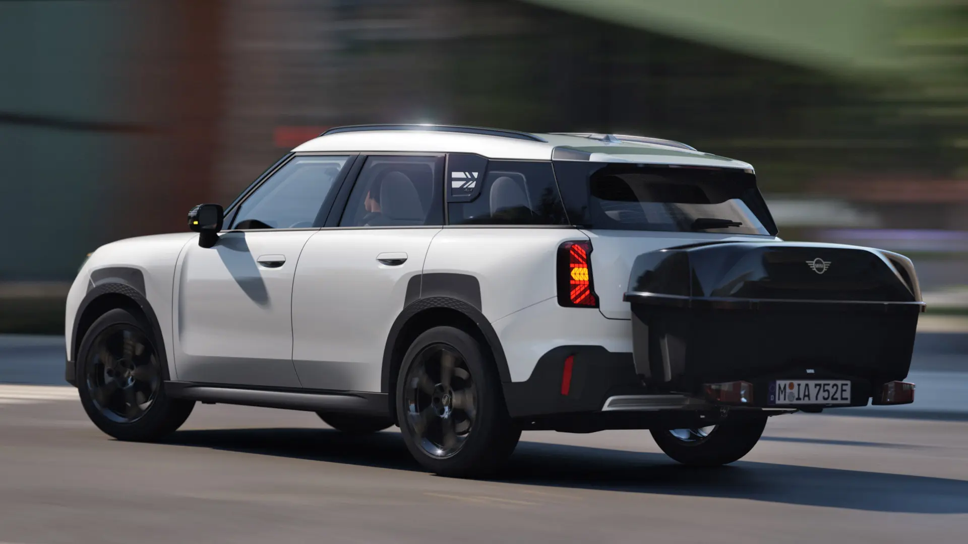 Prikaz stražnjeg kraja MINI Aceman modela u Nanuq White boji opremljen MINI stražnjim nosačem za bicikle i nosi MINI stražnju kutiju. 