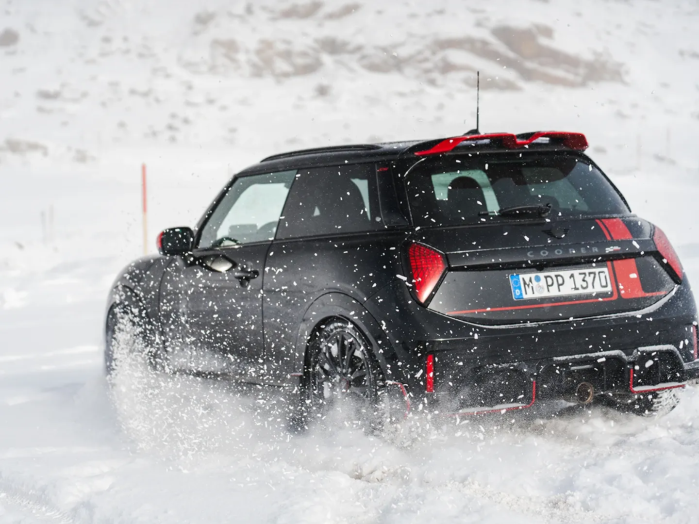 Prikaz stražnjeg kraja MINI Cooper JCW modela koji vozi kroz snijeg.