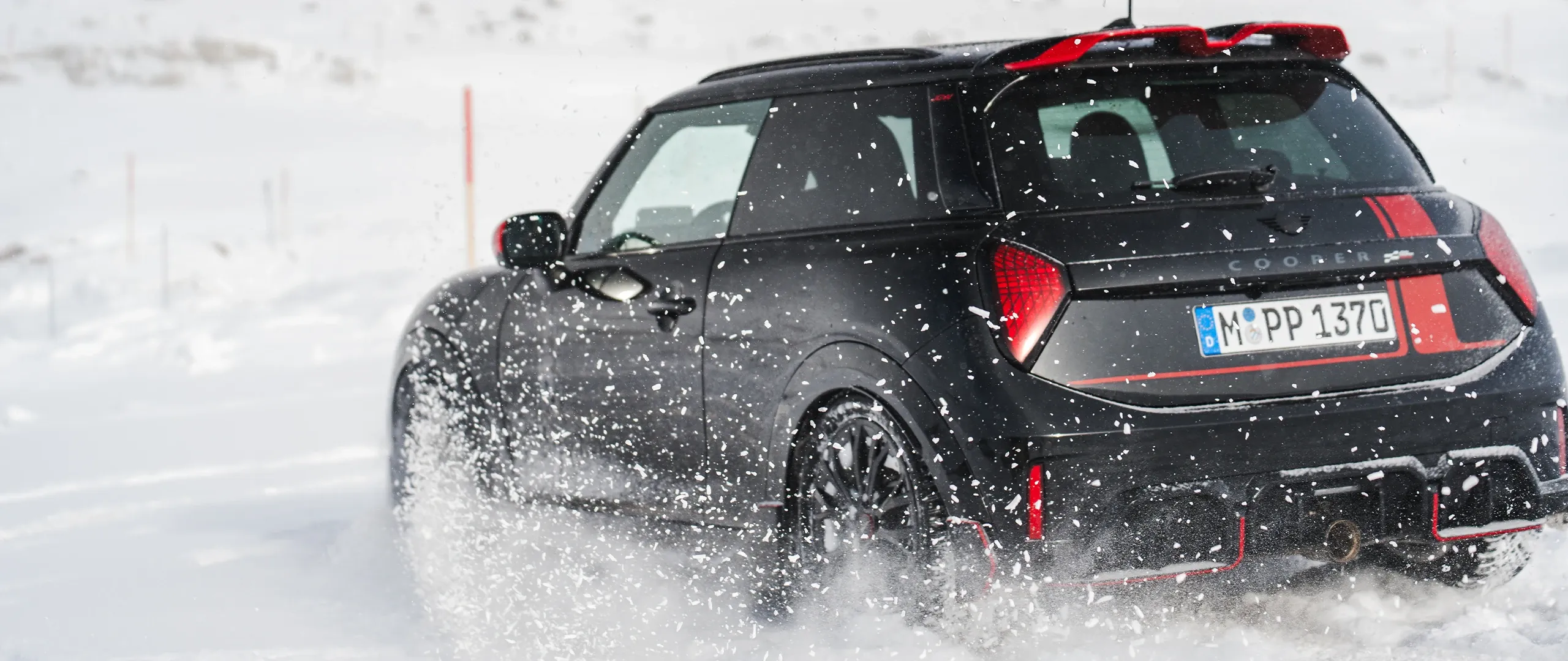 Prikaz stražnjeg kraja MINI Cooper JCW modela koji vozi kroz snijeg.
