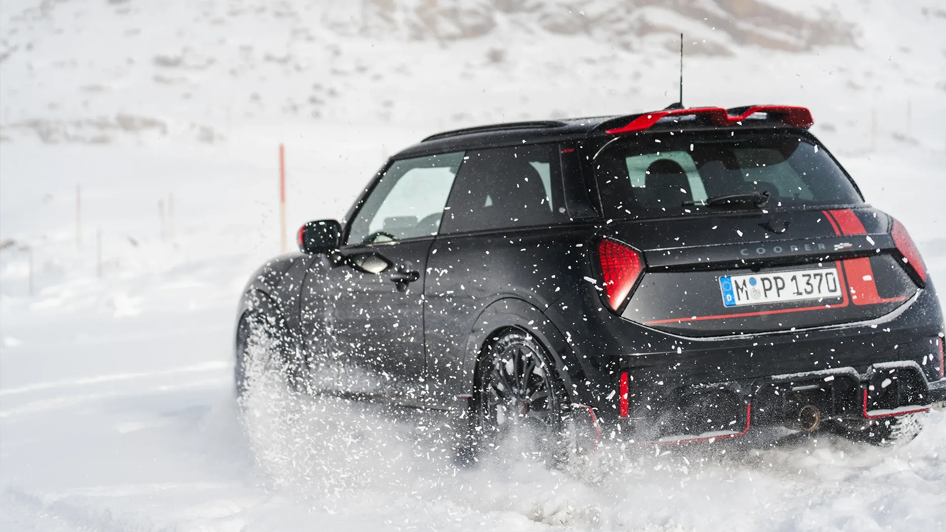 Prikaz stražnjeg kraja MINI Cooper JCW modela koji vozi kroz snijeg.
