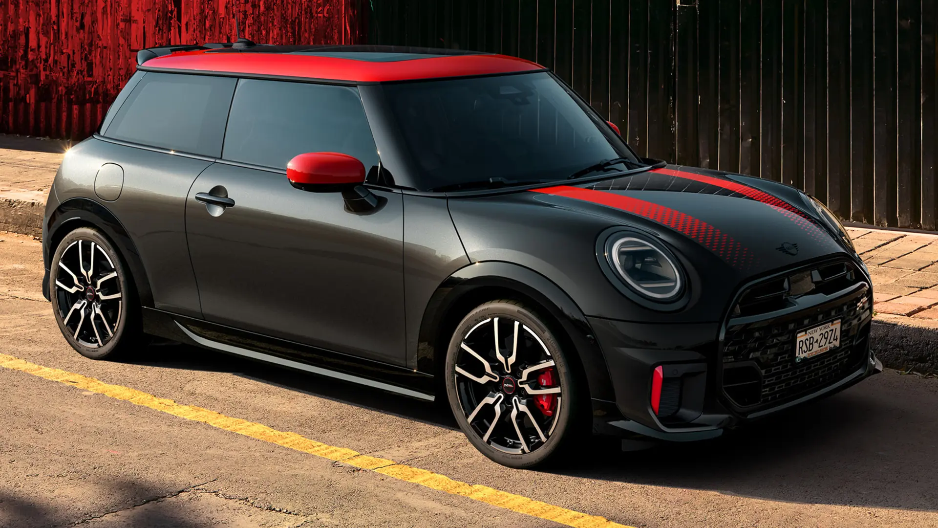 MINI John Cooper Works 3-door u Midnight Black boji s krovom i poklopcima retrovizora u Chilli Red boji i crvenim sportskim prugama, bočni pogled, parkiran na ulici.