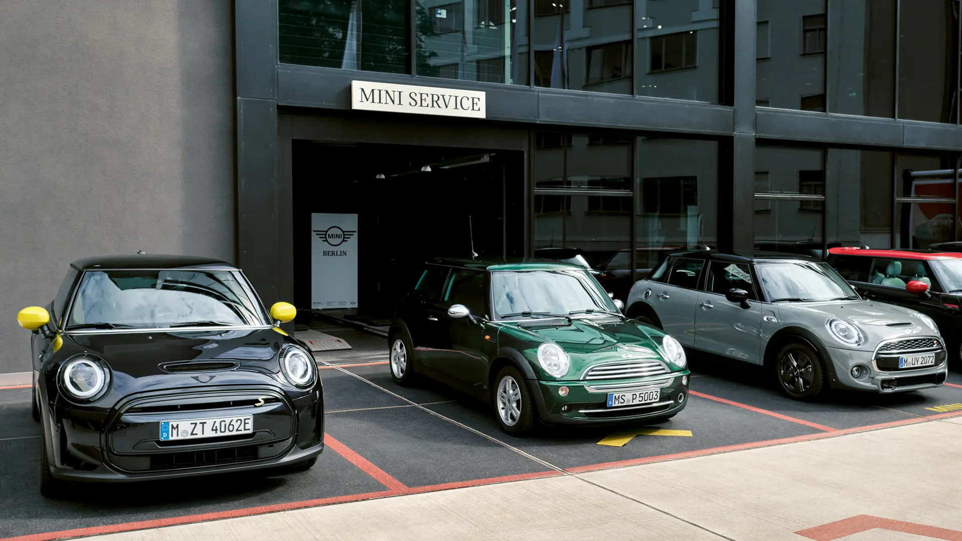 Pogled sprijeda na električni MINI Cooper S u crnoj boji ispred MINI prodajnog centra uz zeleni MINI Cooper 3-vrata, srebrni MINI 5-vrata, i crni MINI JCW  