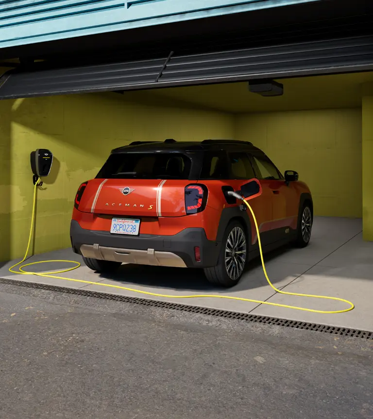 Potpuno električni MINI Aceman S puni se na MINI Wallbox Plus, stražnji pogled, parkiran u garaži. 