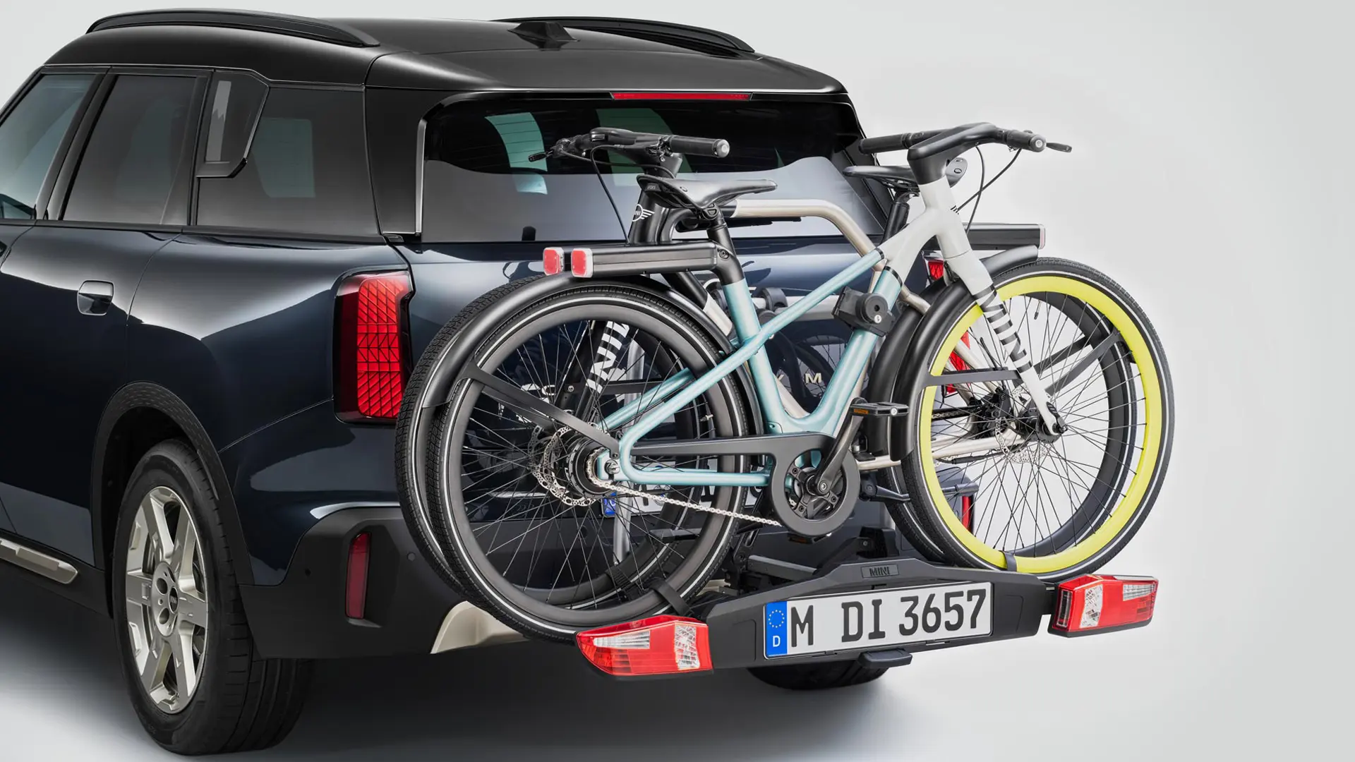 MINI Countryman u crnoj boji sa stražnjim nosačem za bicikle, i dva pričvršćena brdska bicikla, pogled straga. 