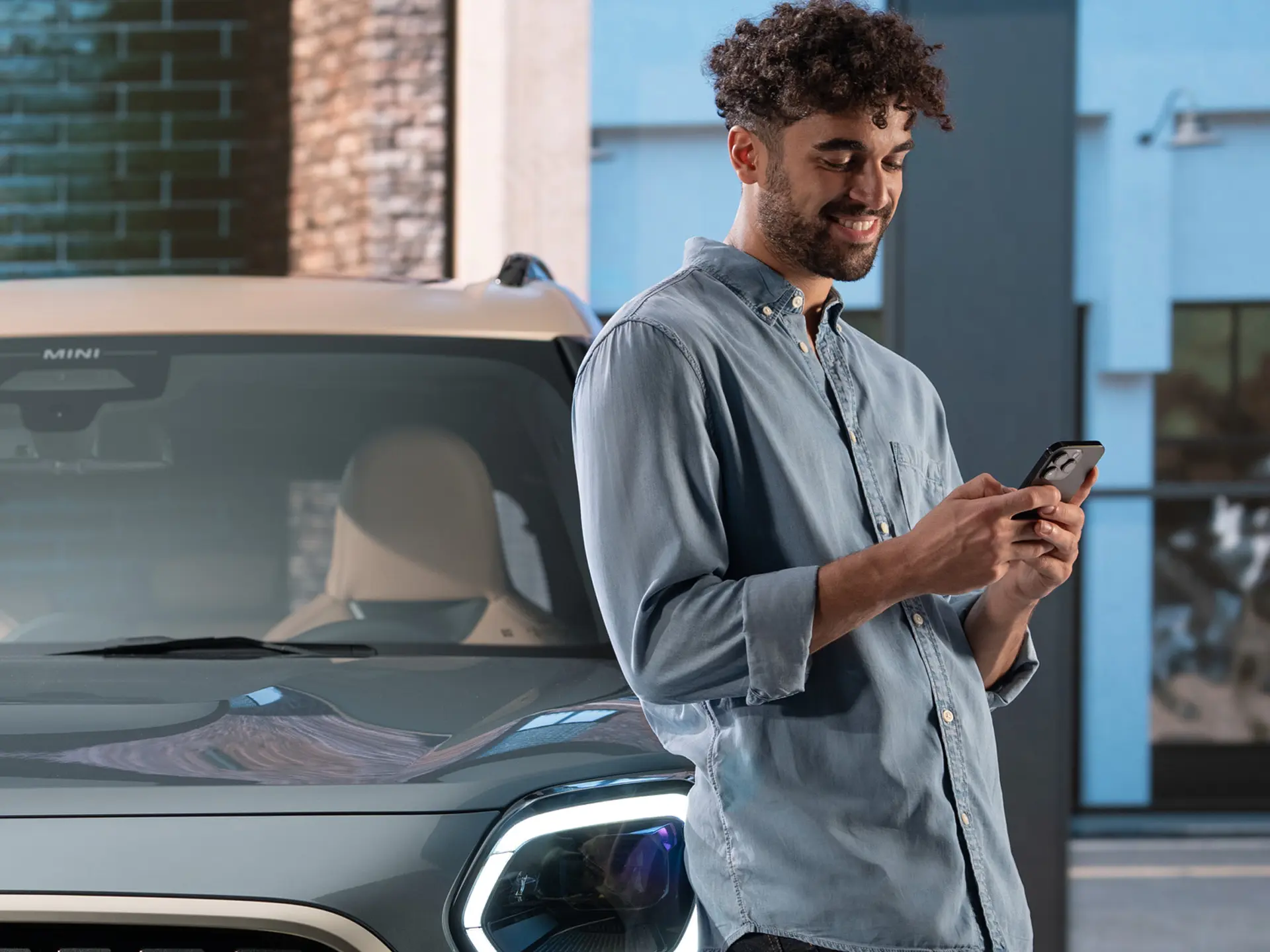 MINI personalizirani termini za servis - muškarac tipka na svom telefonu pored MINI-ja